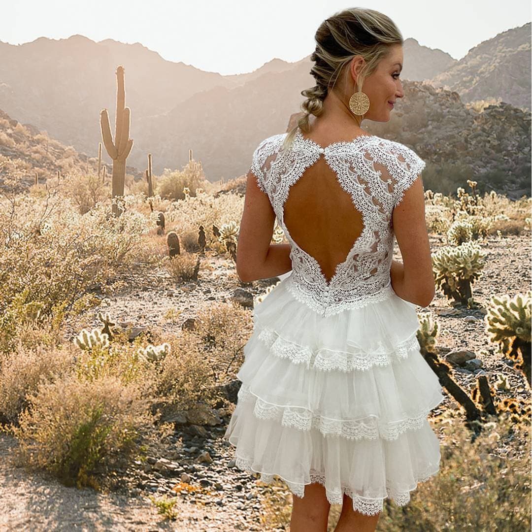 Woman in a short white lace wedding dress standing in a desert landscape
