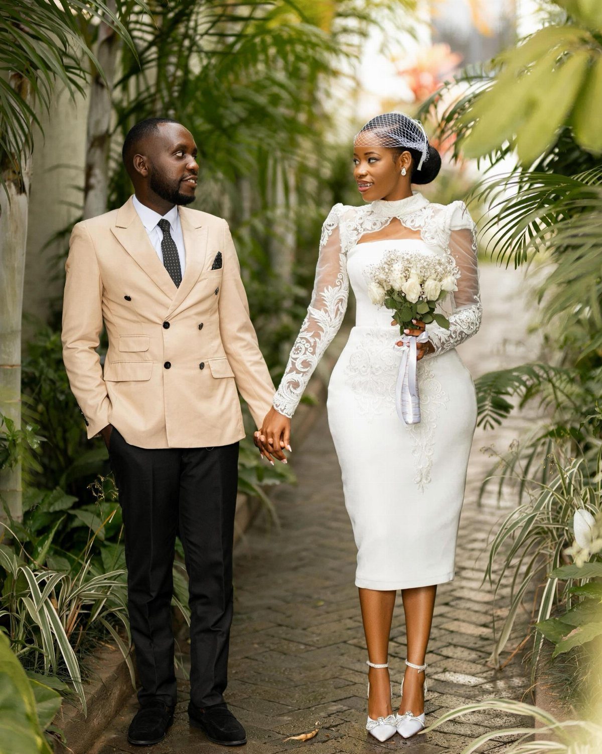 Couple in wedding attire holding hands in a tropical garden setting