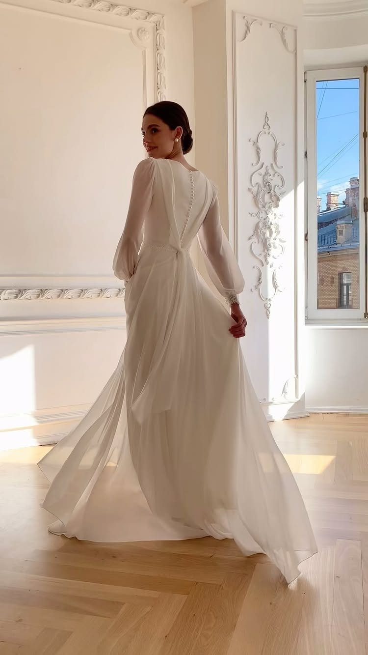 Woman in a long sleeve white wedding dress standing in a bright room