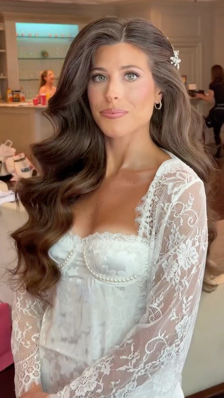 Woman with long wavy brown hair and a floral clip wearing white lace