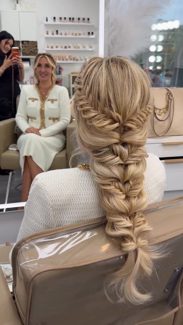 Long blonde hair styled in a thick, textured bridal braid cascading down the back.