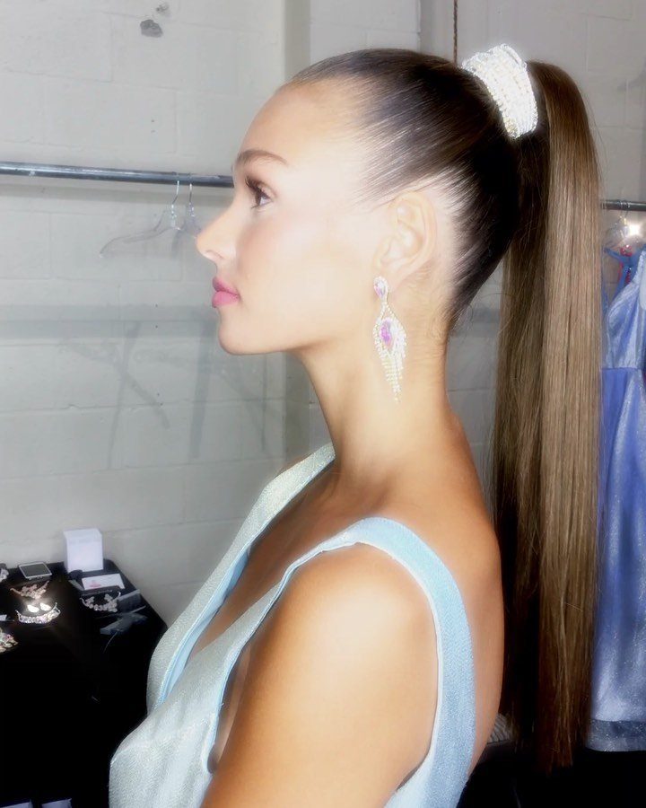 Woman with a high sleek ponytail and white scrunchie wearing a blue dress.