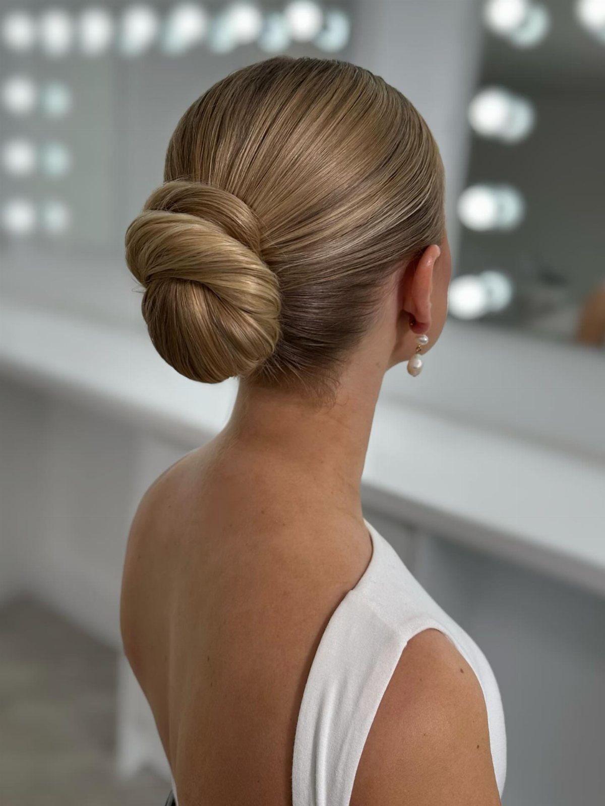 Blonde woman with a smooth slicked-back low bun and pearl earring in studio