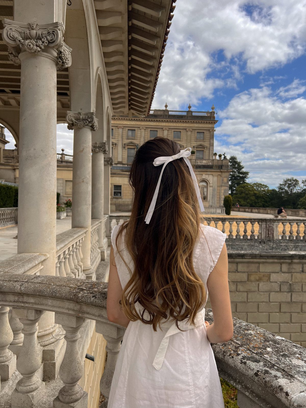 Woman with long wavy brown hair and a white bow at a palace