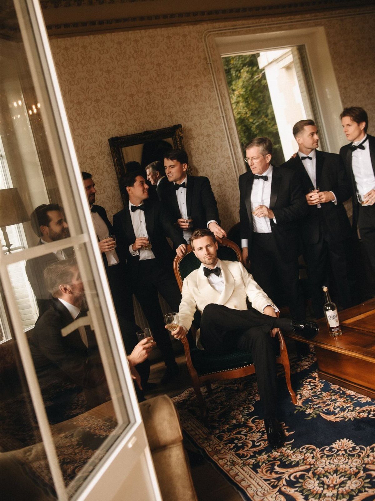 Men in formal black tuxedos and one white dinner jacket posing in a room.