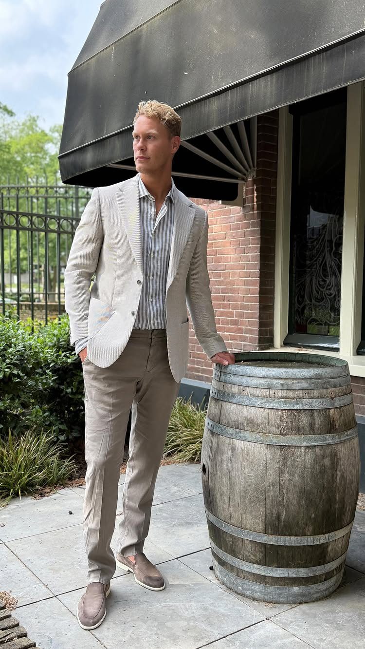 Man in light beige blazer and tan trousers posing by a wooden barrel.