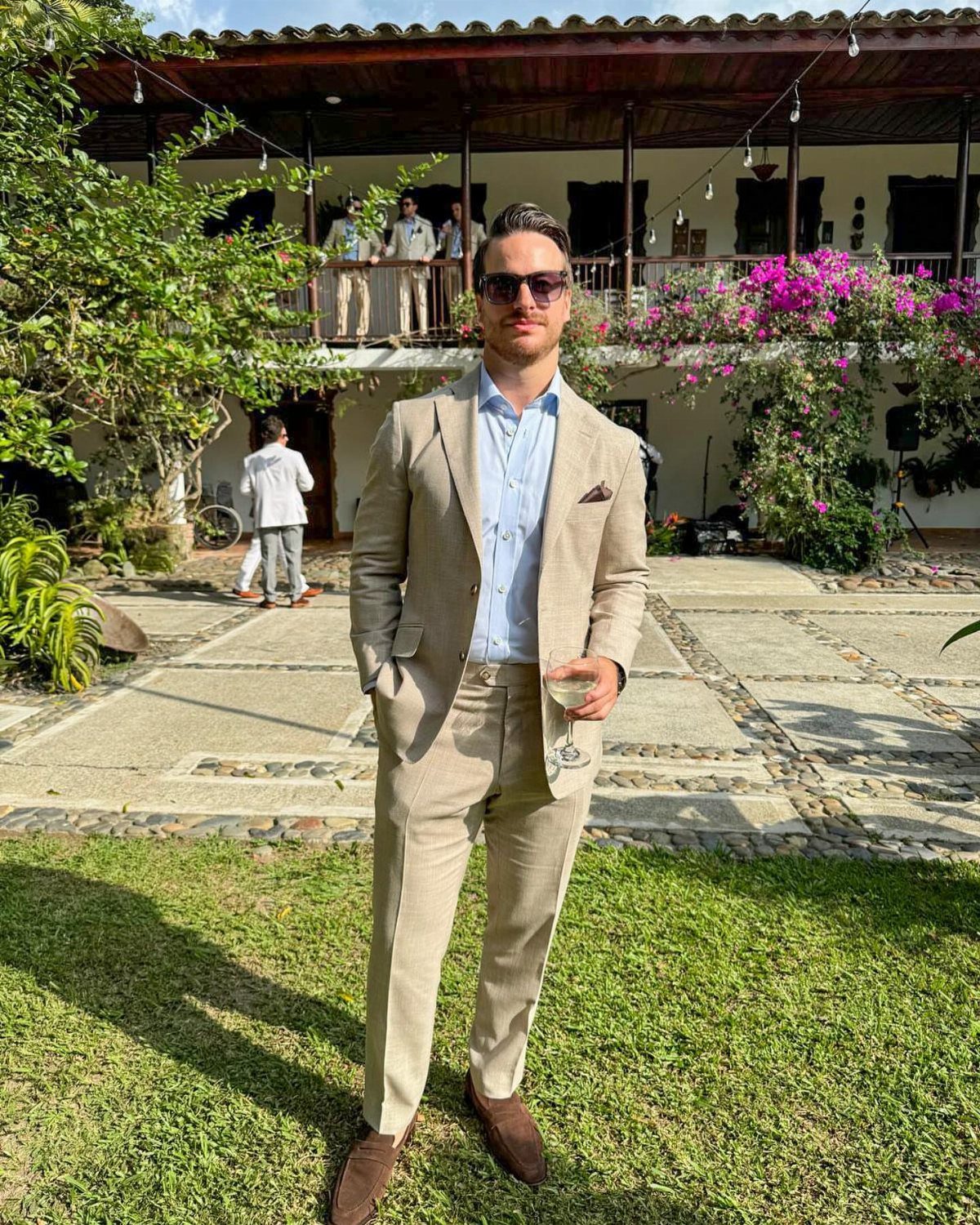 Man wearing a light beige linen suit and brown loafers standing on a lawn