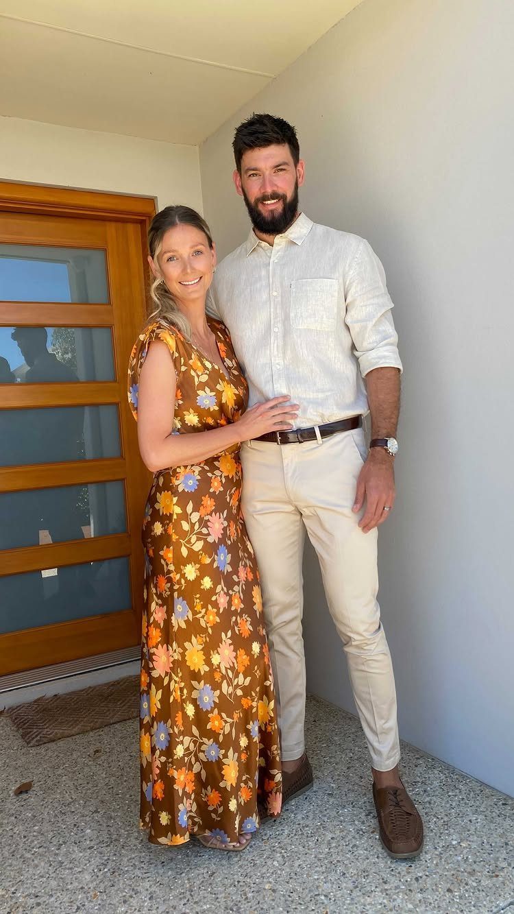 Man in white shirt and beige chinos posing with woman in floral dress.