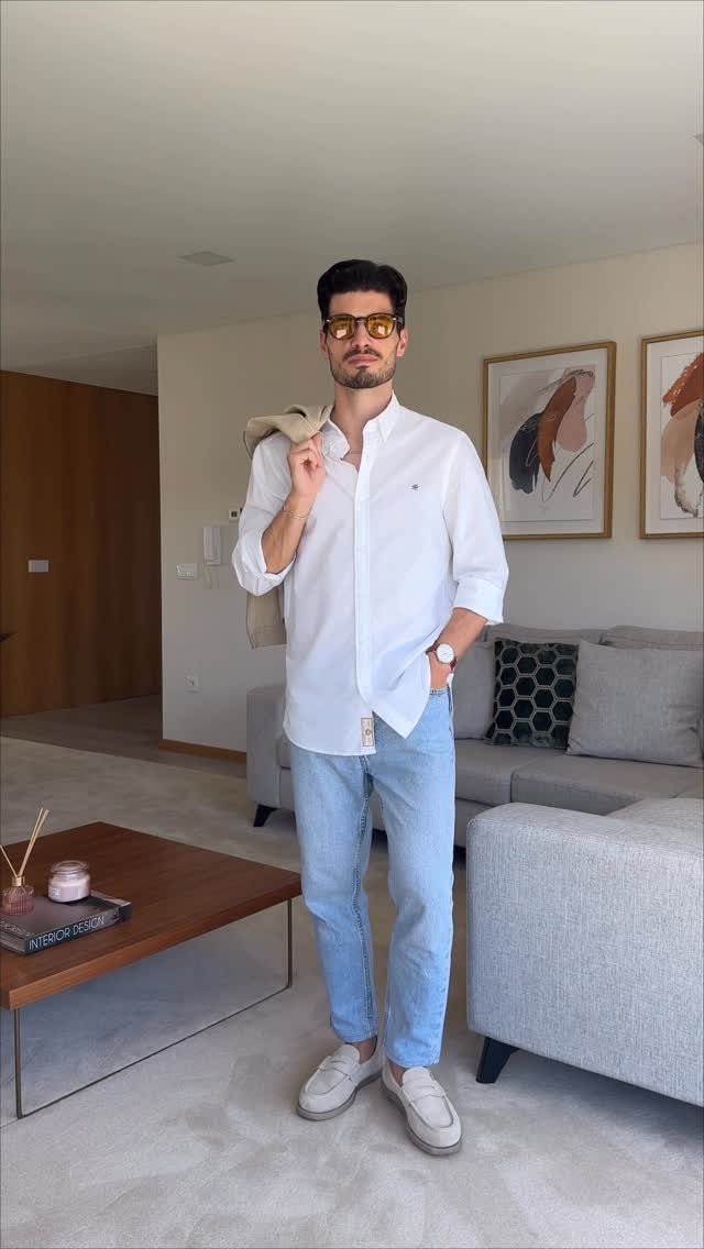 Man in white shirt and light blue trousers holding a beige blazer.