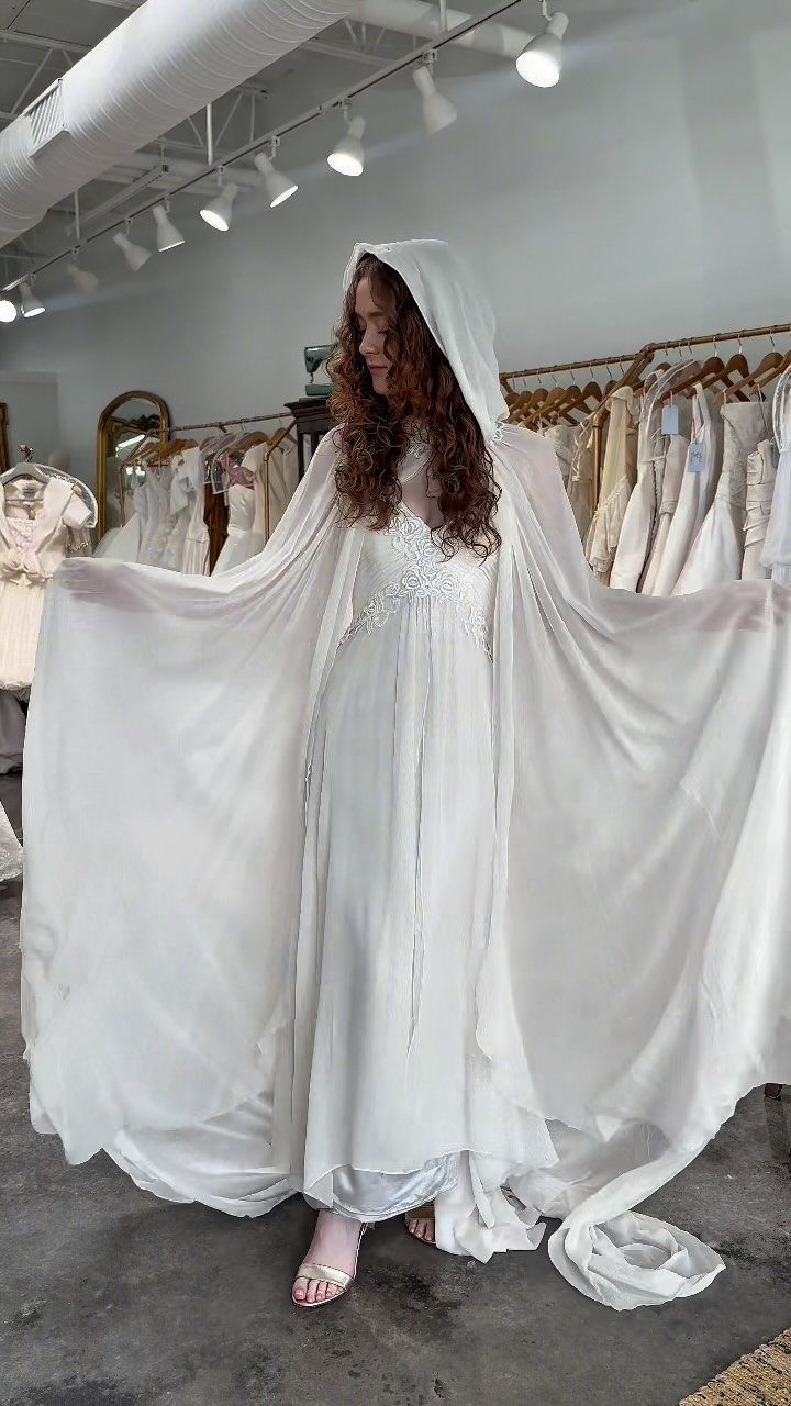 Woman wearing a white hooded vintage wedding gown inside a bridal boutique shop.