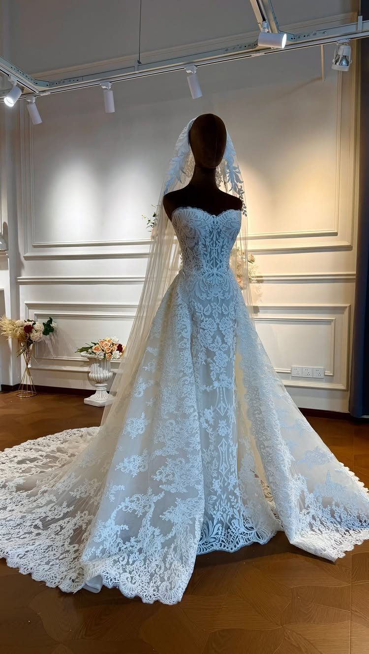 White lace wedding dress with a long train on a mannequin in a boutique.