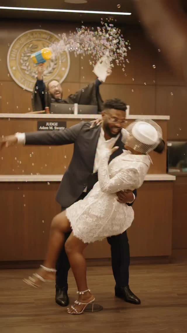 Couple embracing in a courtroom, woman wearing a short vintage style white lace dress