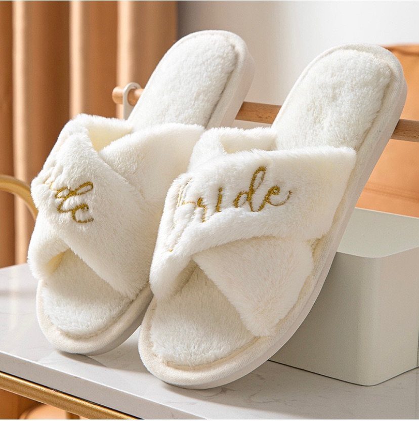 White fluffy bridal slippers with gold Bride embroidery on a marble surface