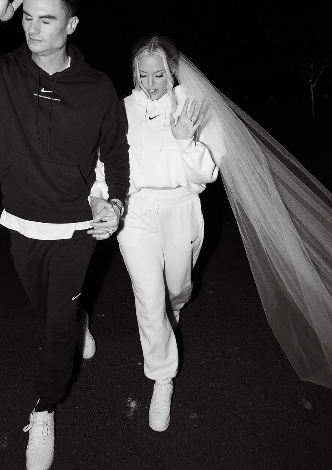 Couple walking at night, woman wearing white Nike athleisure and a bridal veil.