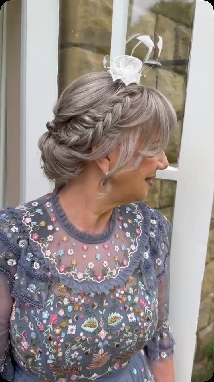 Woman with grey braided updo and white fascinator wearing a floral grey dress.