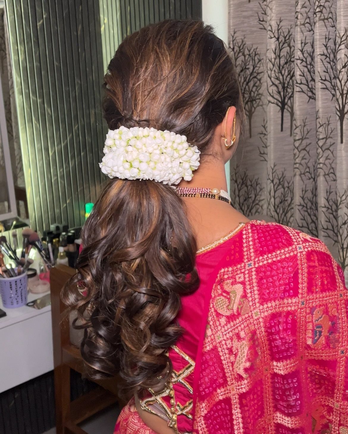 Woman with curly low ponytail adorned with white flowers wearing pink embroidered saree