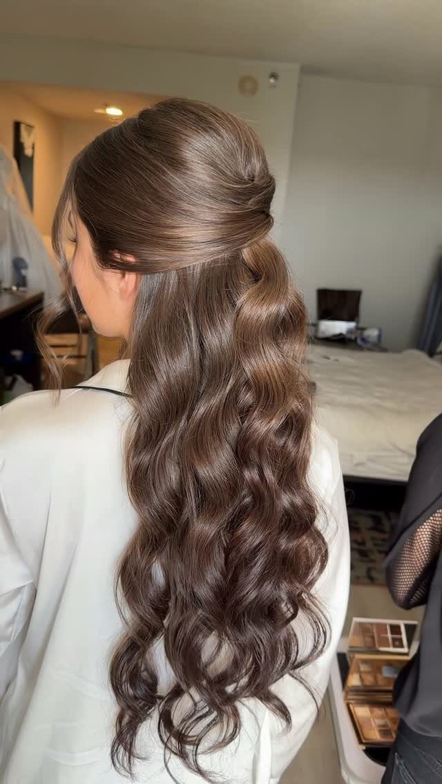 Woman with long brown hair in a half-up hairstyle with loose curls.