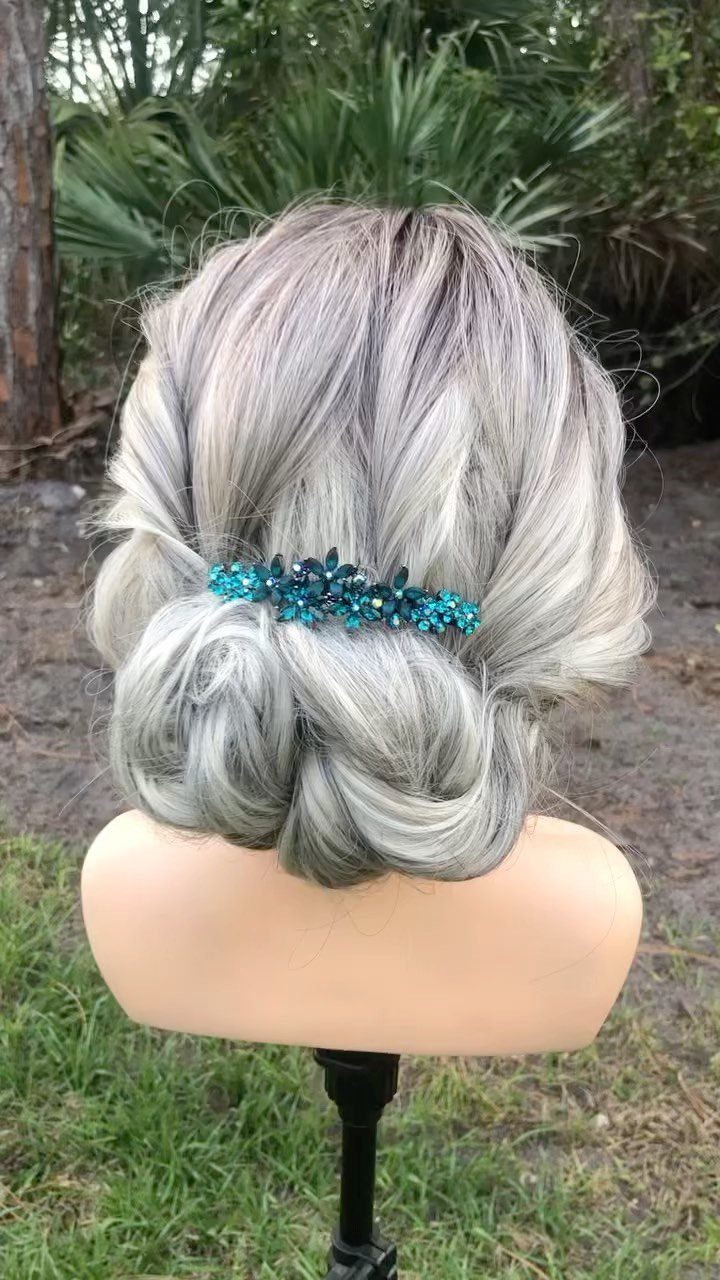 Silver-grey hair in a textured low bun with a blue jeweled hair clip.