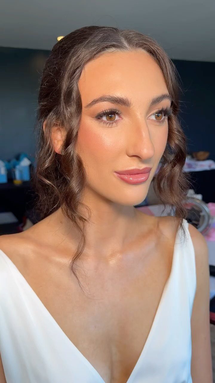 Woman in white dress with glowing, sun-kissed bridal makeup and wavy brown hair.