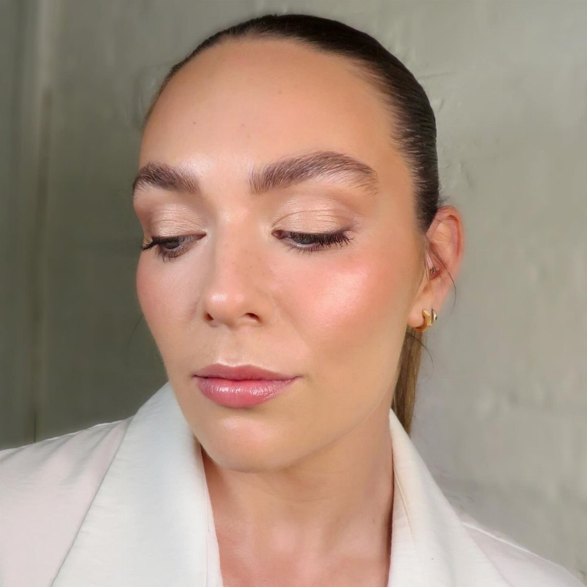 Woman with natural bridal makeup, shimmering eyeshadow, and glossy lips wearing white blazer