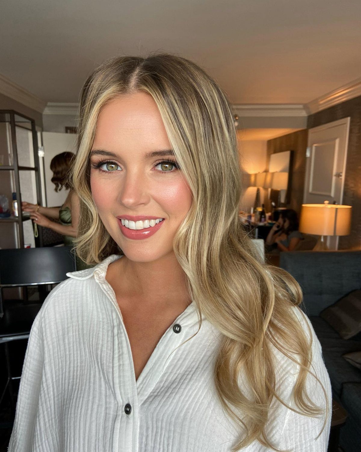 Smiling woman with blonde wavy hair wearing natural bridal makeup and white shirt.