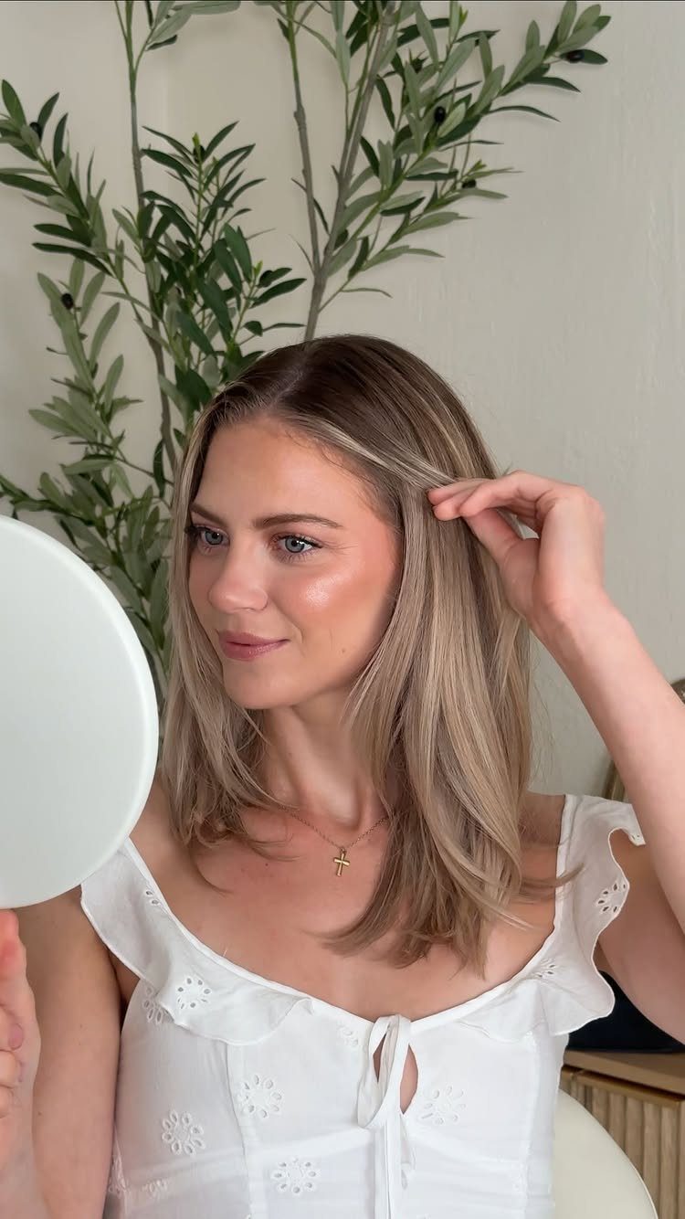 Woman with soft neutral makeup and blonde hair looking into a small mirror.