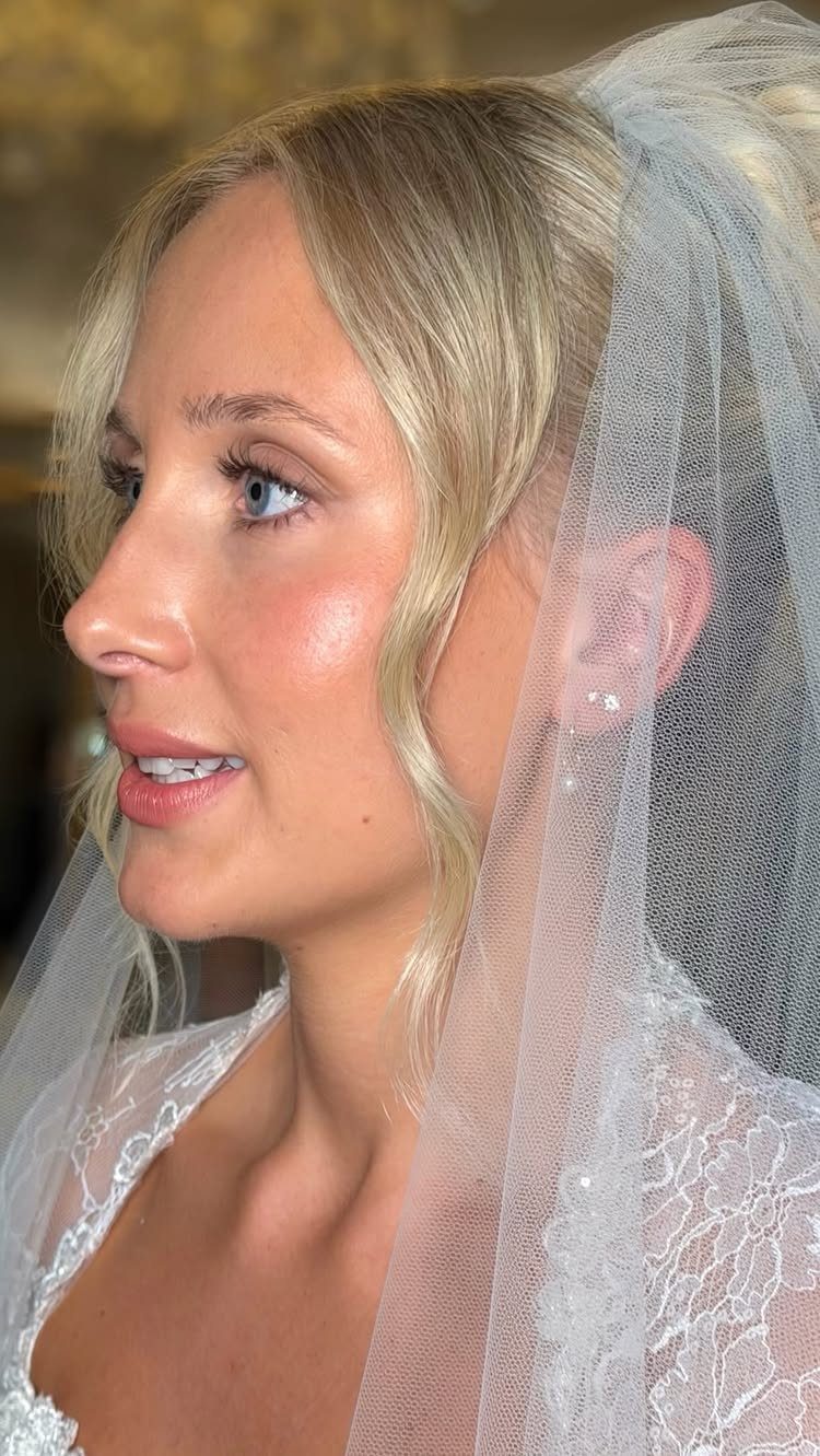 Blonde bride in white lace dress and veil with glowing natural makeup.