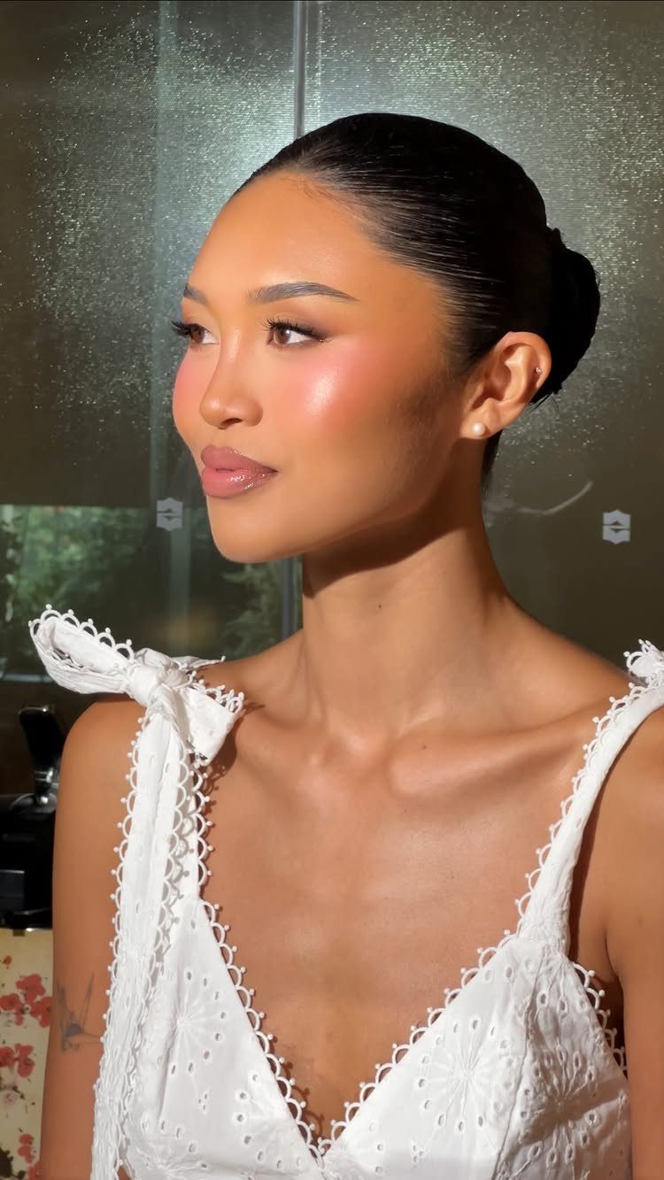 Woman in white lace dress with glowing bridal makeup and defined neutral eyes.