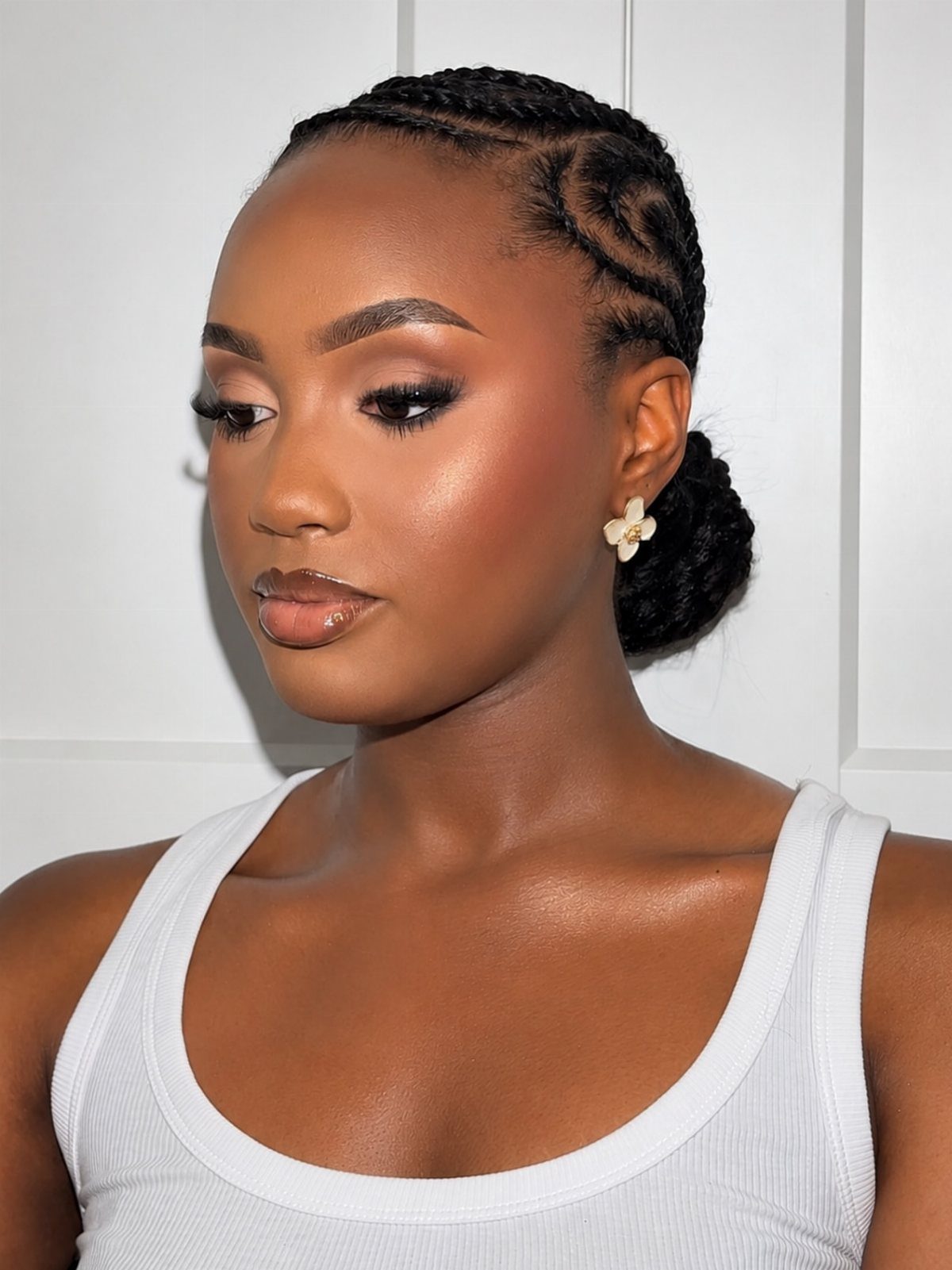 Woman with glowing skin, braided hair, and soft glam makeup wearing white tank top
