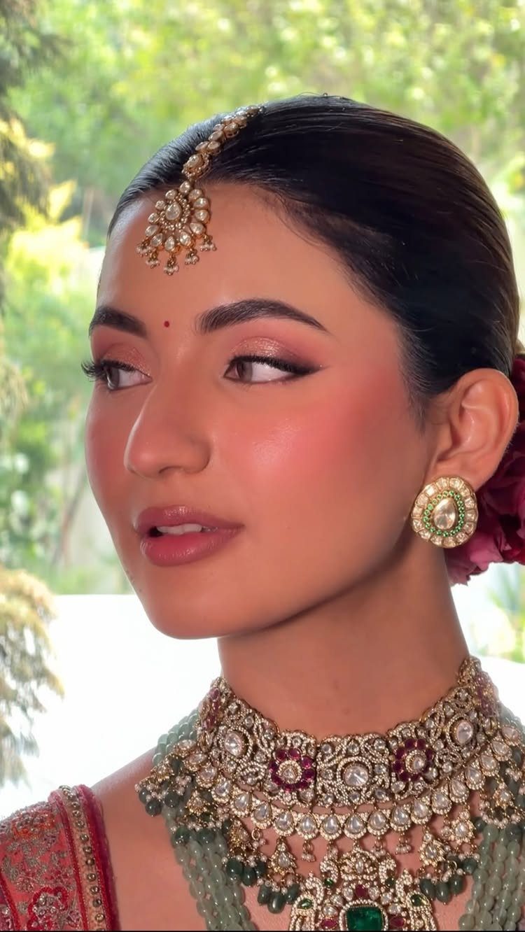 Woman with fair skin wearing natural bridal makeup and ornate gold Indian jewelry.