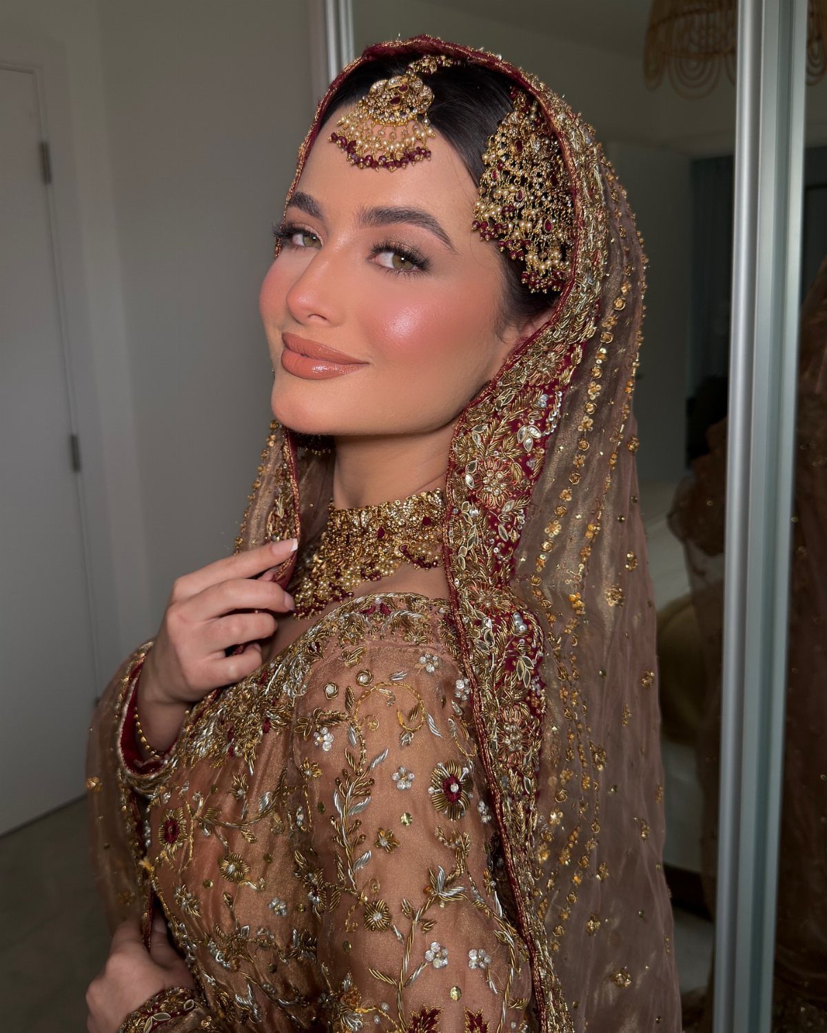 Woman in gold bridal attire with peachy makeup and traditional gold jewelry.