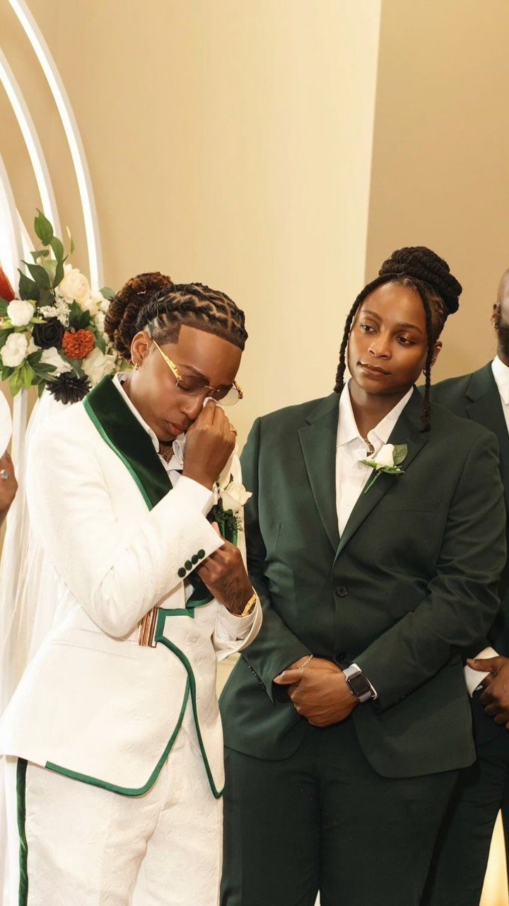 Two people in non-traditional wedding suits, one white with green and one dark green.