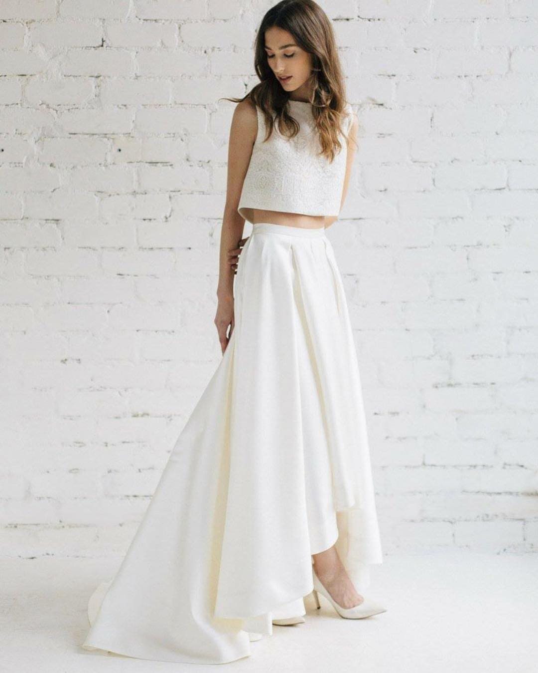 Woman wearing a white cropped bridal top and high-low skirt against brick wall