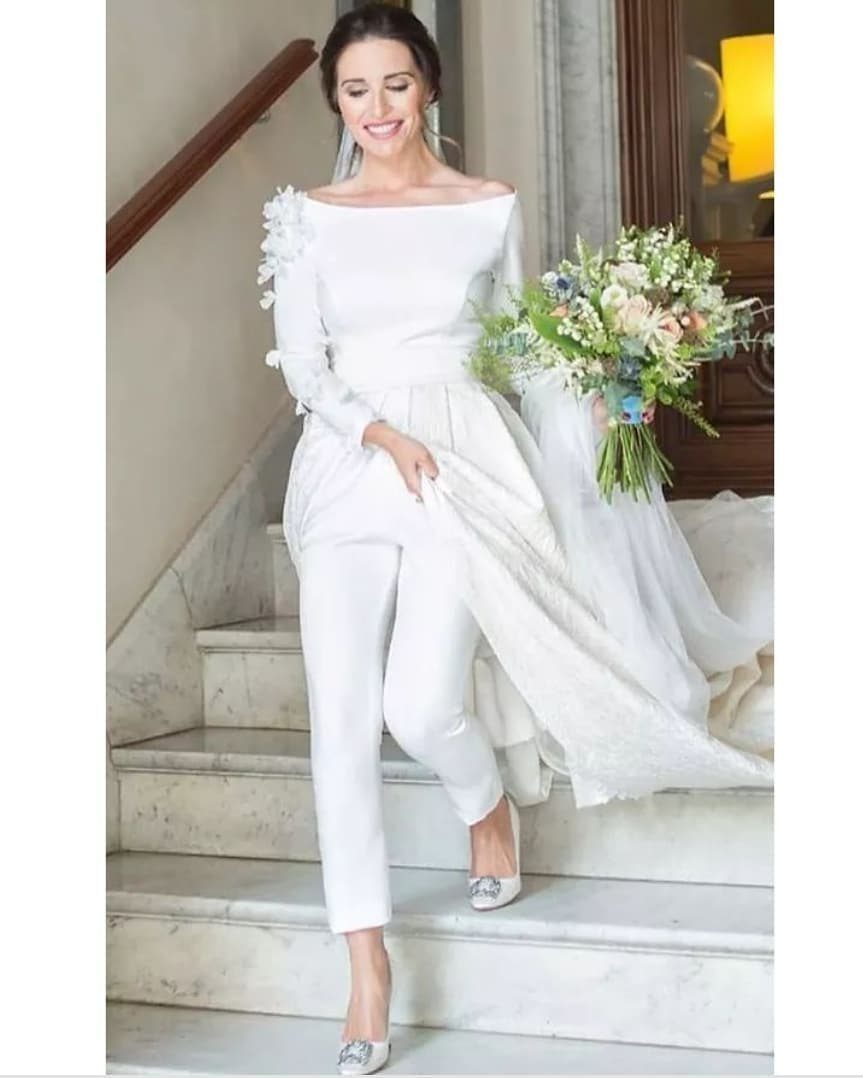 Woman in a white off-the-shoulder wedding jumpsuit with a train and floral bouquet.