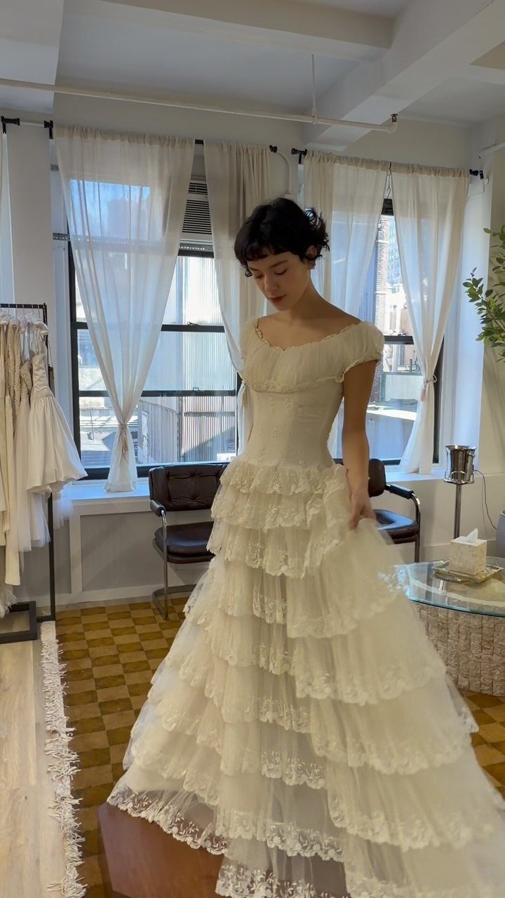 Woman wearing a white off-the-shoulder vintage wedding dress with tiered lace ruffles.