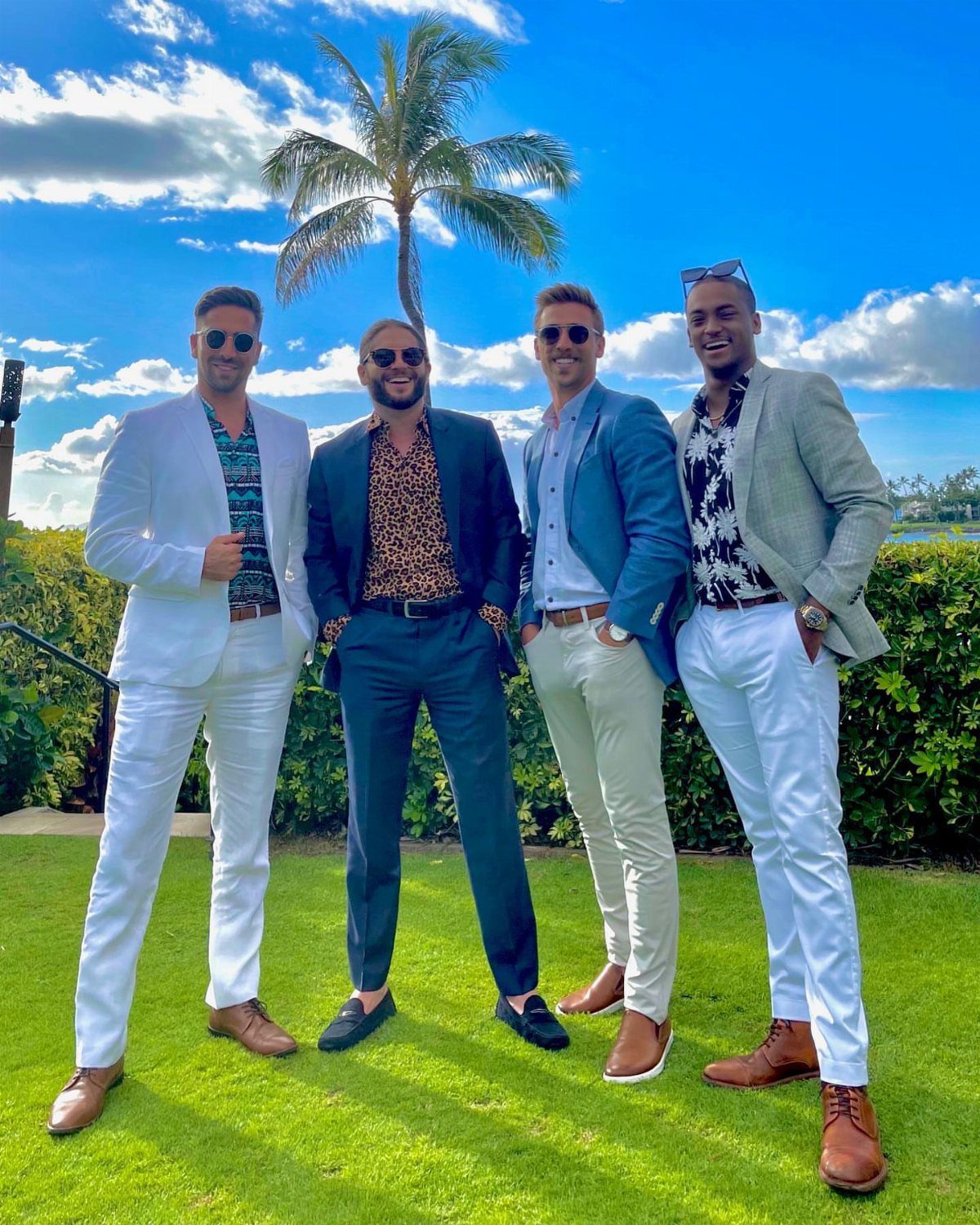 Four men in smart casual blazers and dress shirts posing on a sunny lawn.