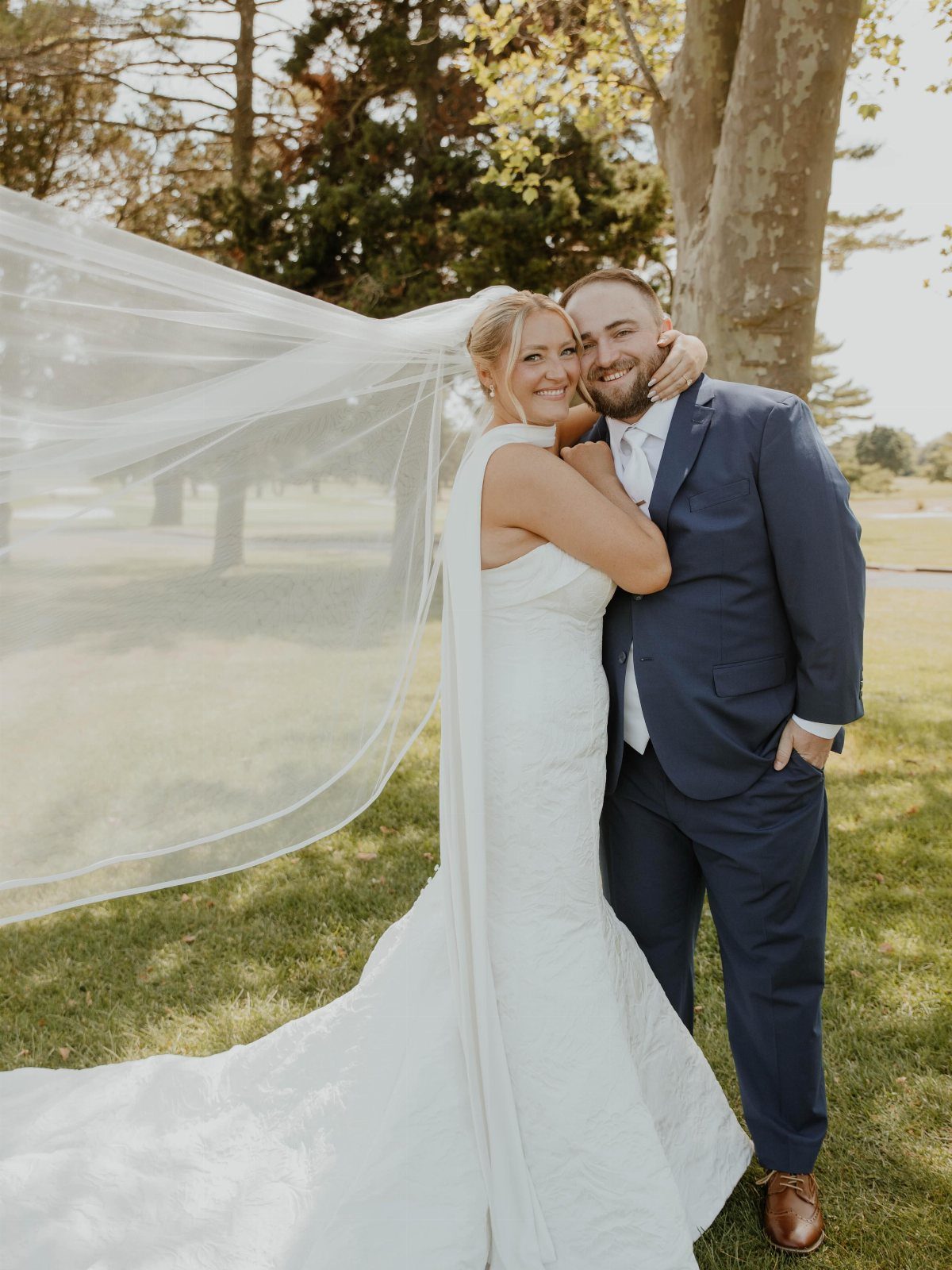 Bride and groom posing outdoors, groom wearing a navy blue wedding suit.