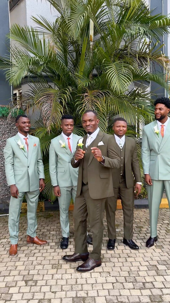 Five men in sage green and olive brown suits posing outdoors by a palm tree.