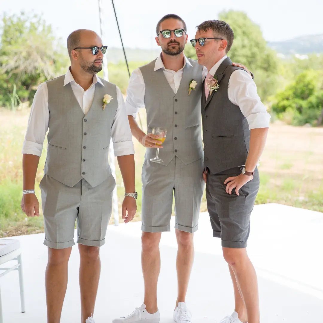 Three men wearing grey short suits with waistcoats and tailored shorts outdoors.