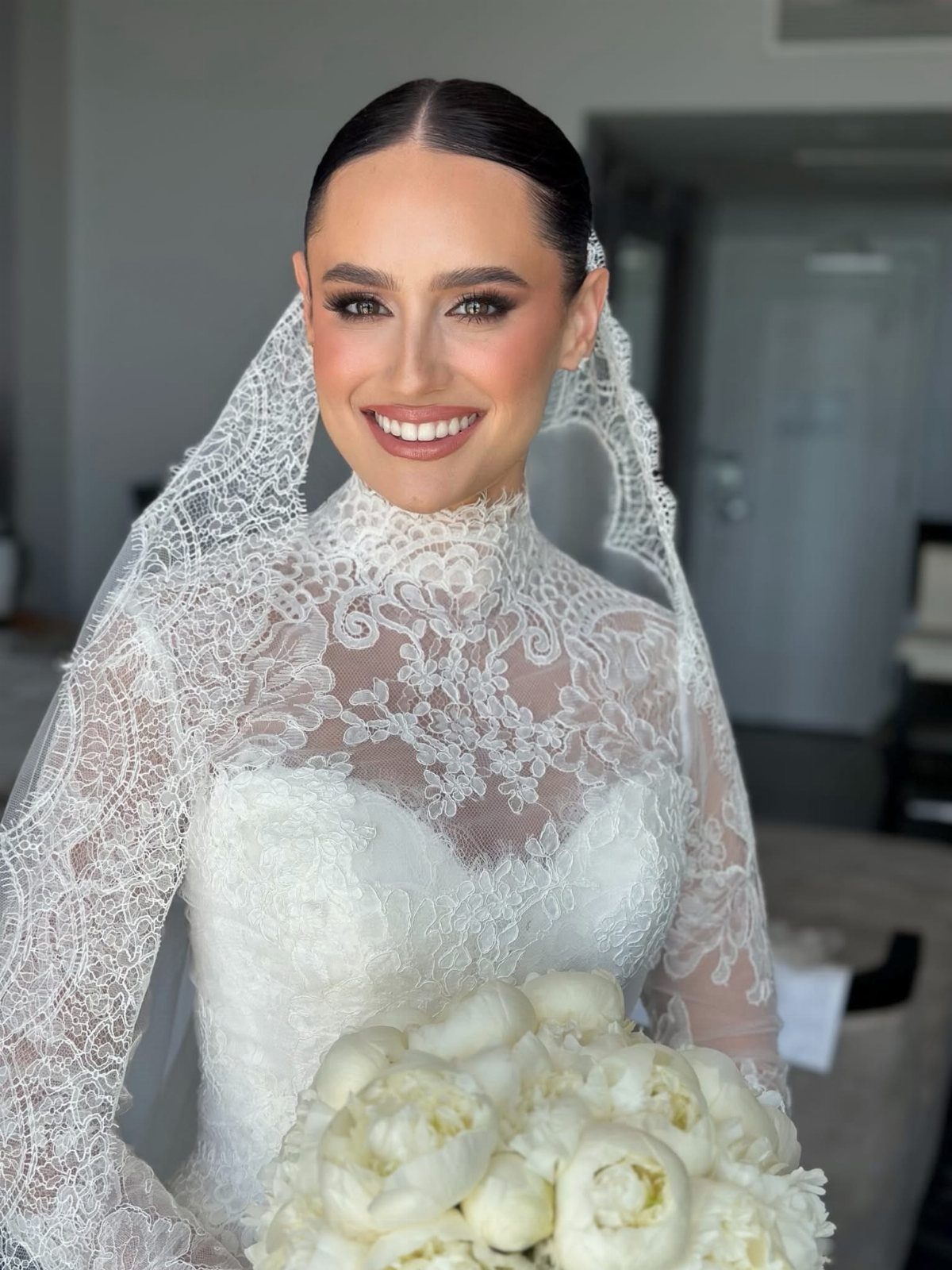 Bride in a white lace wedding dress and veil holding white peonies.