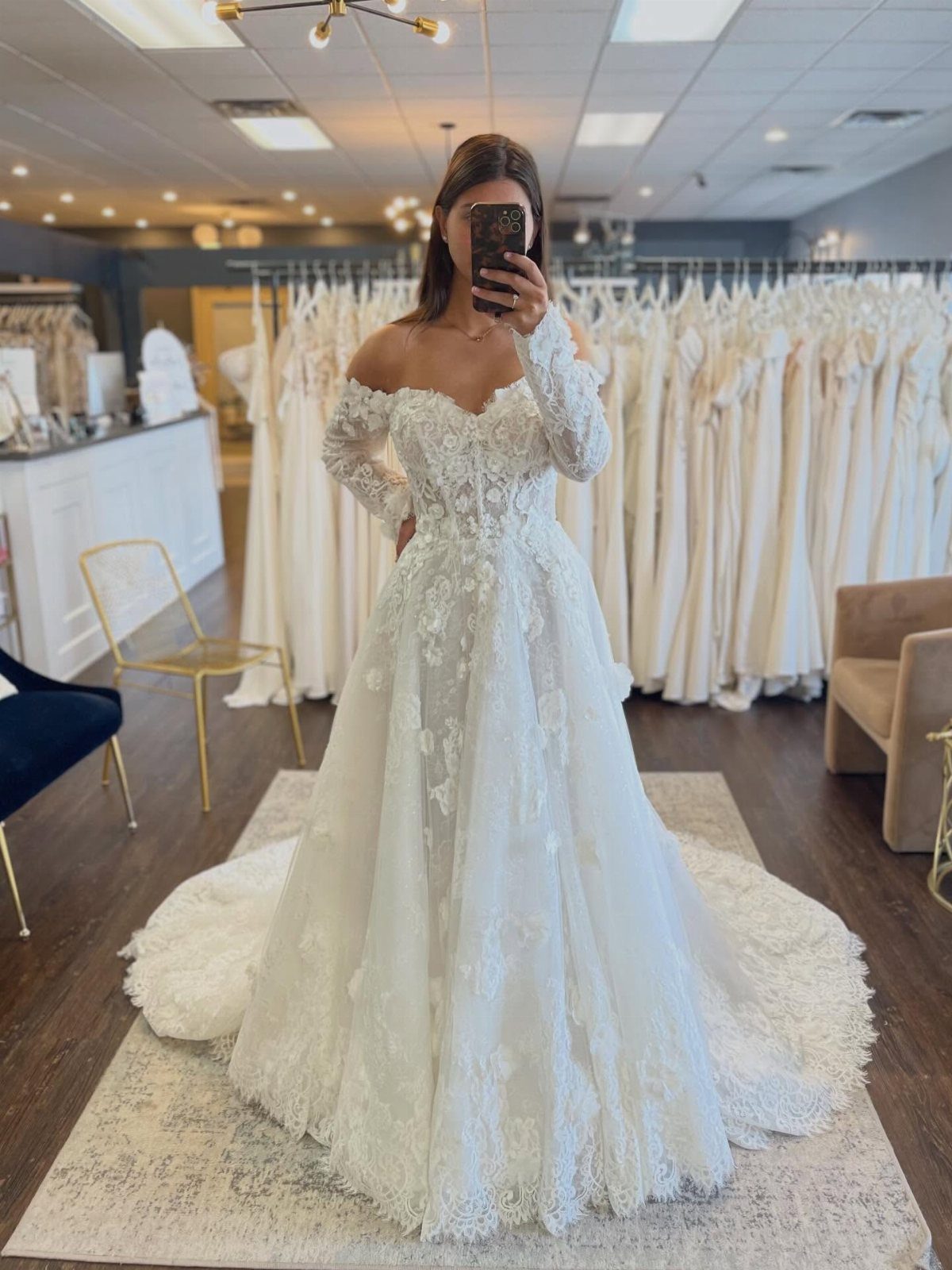 Woman in a white lace off-the-shoulder wedding dress posing in a bridal boutique.