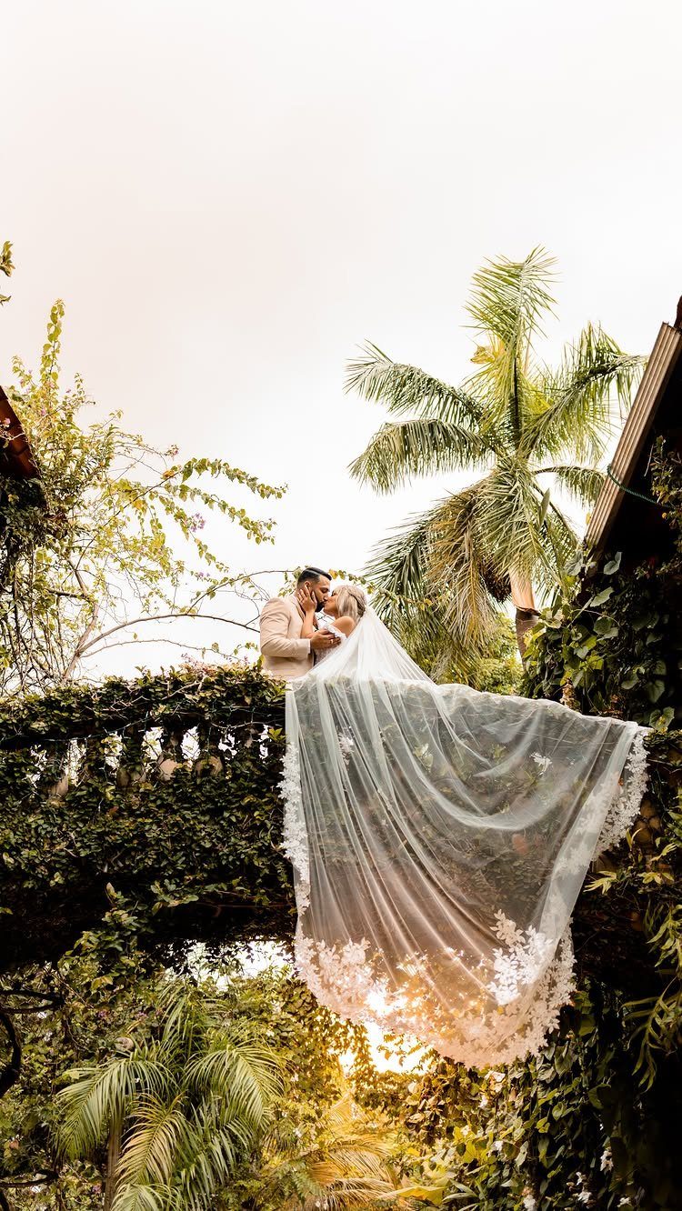 Bride in white lace wedding dress and long veil kissing groom on balcony