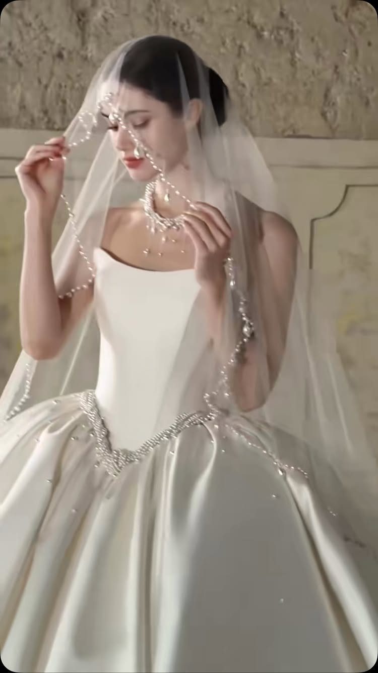 Woman in a voluminous white satin ball gown wedding dress with a pearl veil.
