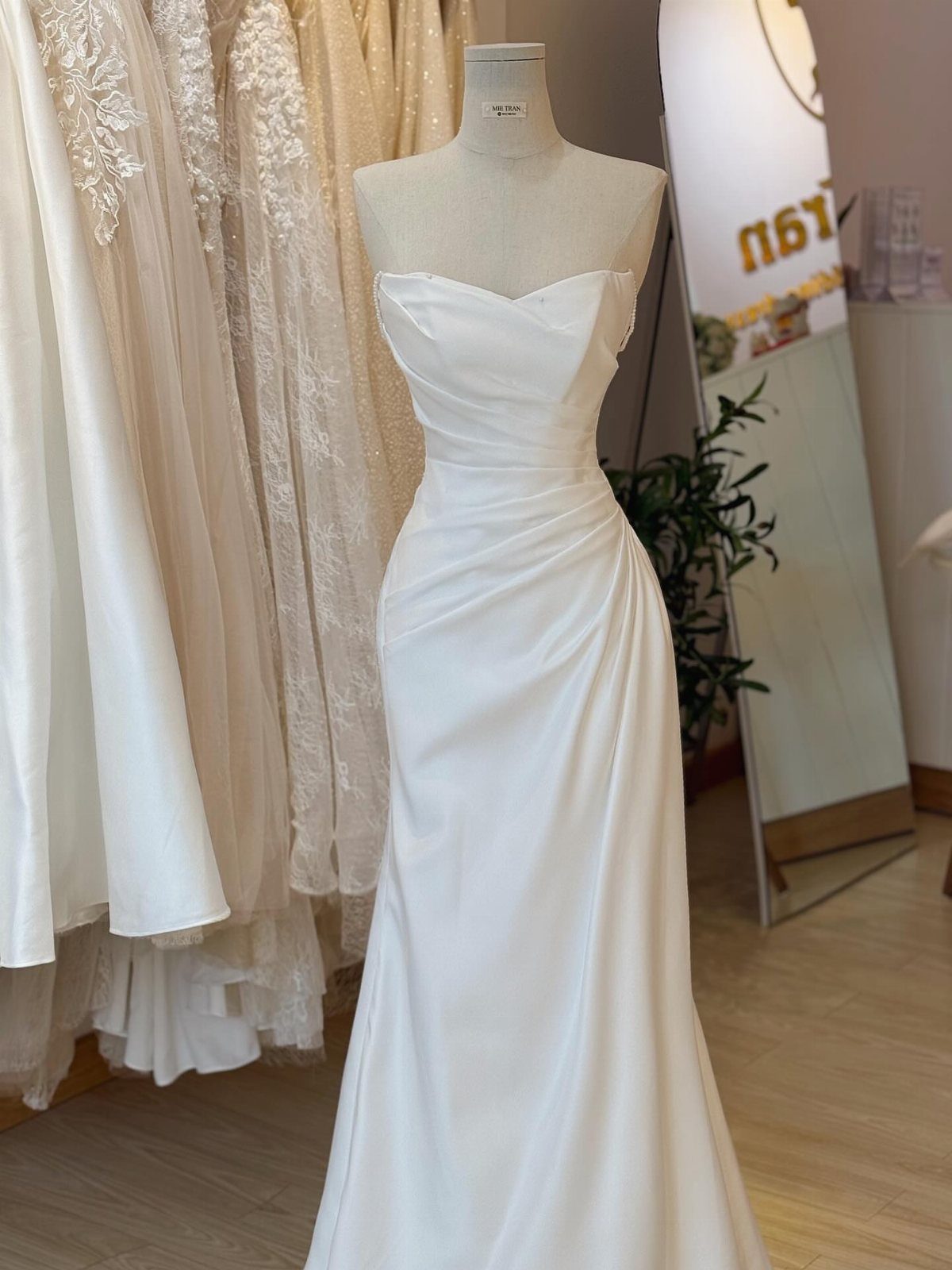 White satin strapless wedding dress with a draped bodice on a mannequin.