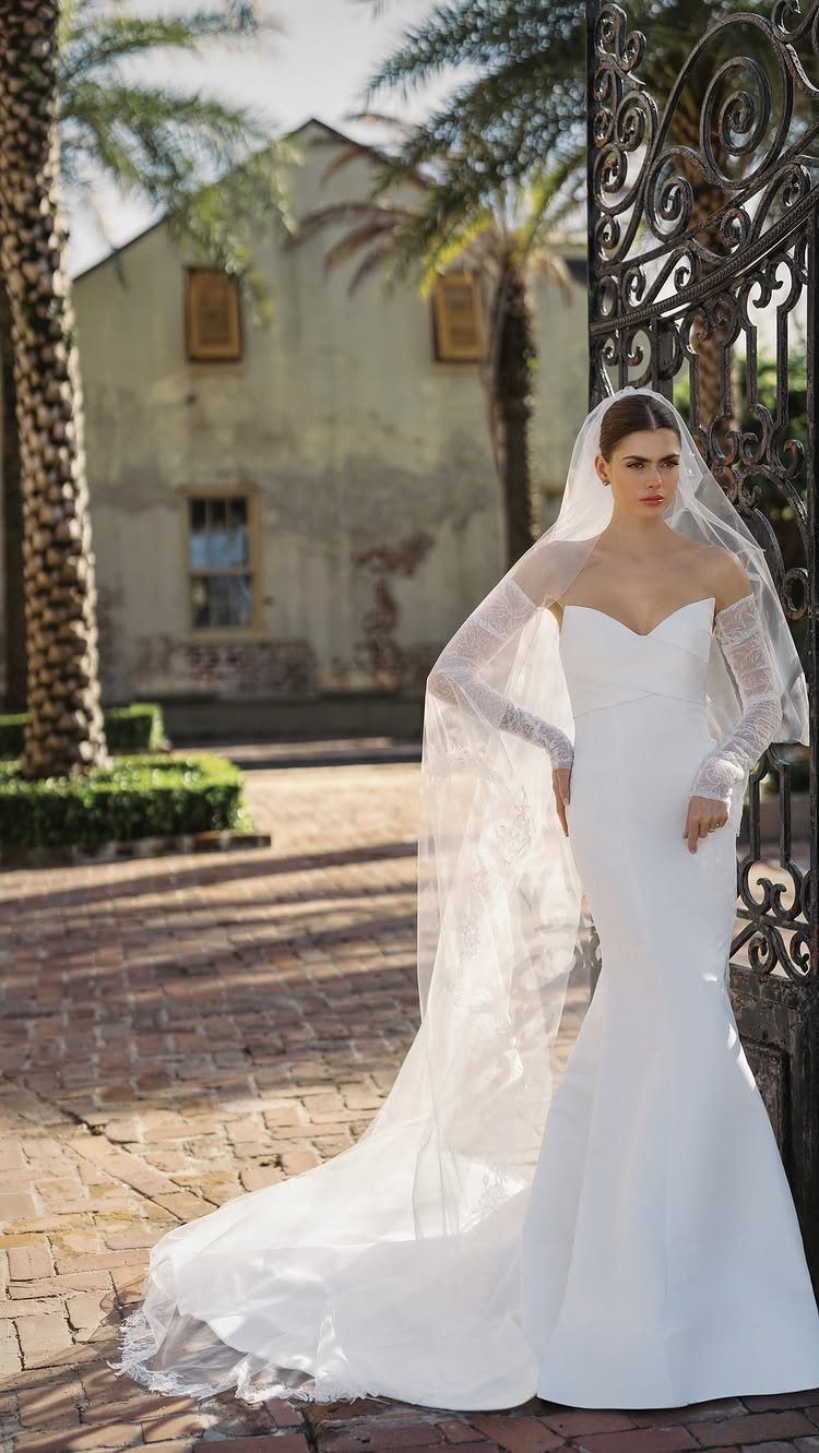 Woman in a white satin fit and flare wedding dress standing by iron gates.