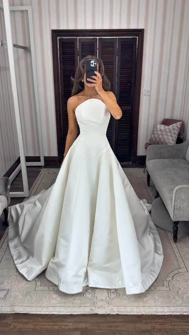 Woman in a white strapless satin A-line wedding dress taking a mirror selfie.
