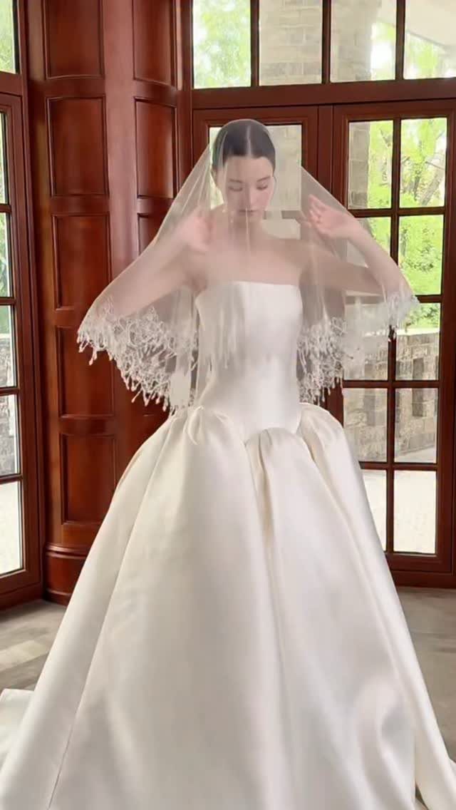 Woman in a strapless white satin princess wedding dress wearing a lace veil.