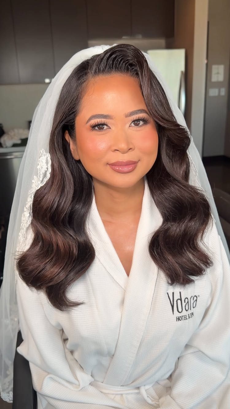 Woman with Hollywood waves and soft glam makeup wearing a bridal veil and robe.