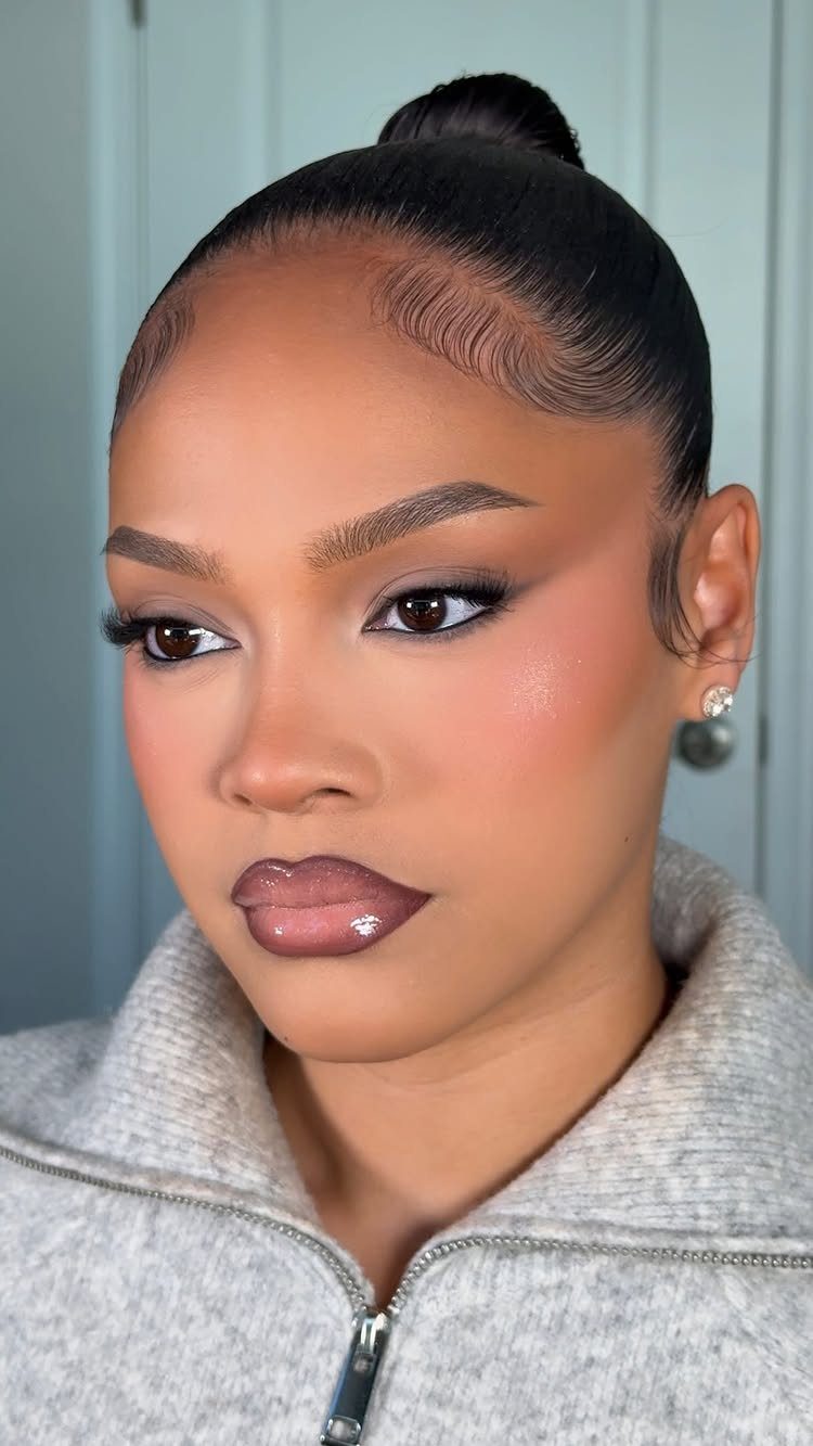 Woman with soft smokey eye makeup, nude glossy lips, and sleek hair bun.
