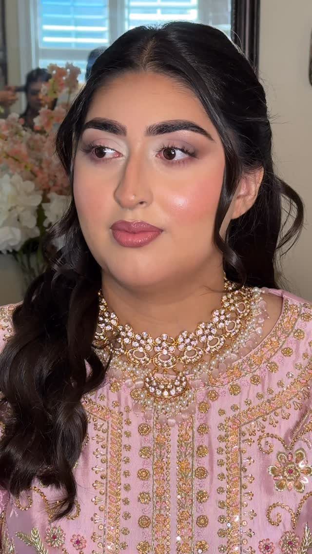 Woman with soft glam bridal makeup, wavy dark hair, and pink embroidered attire.